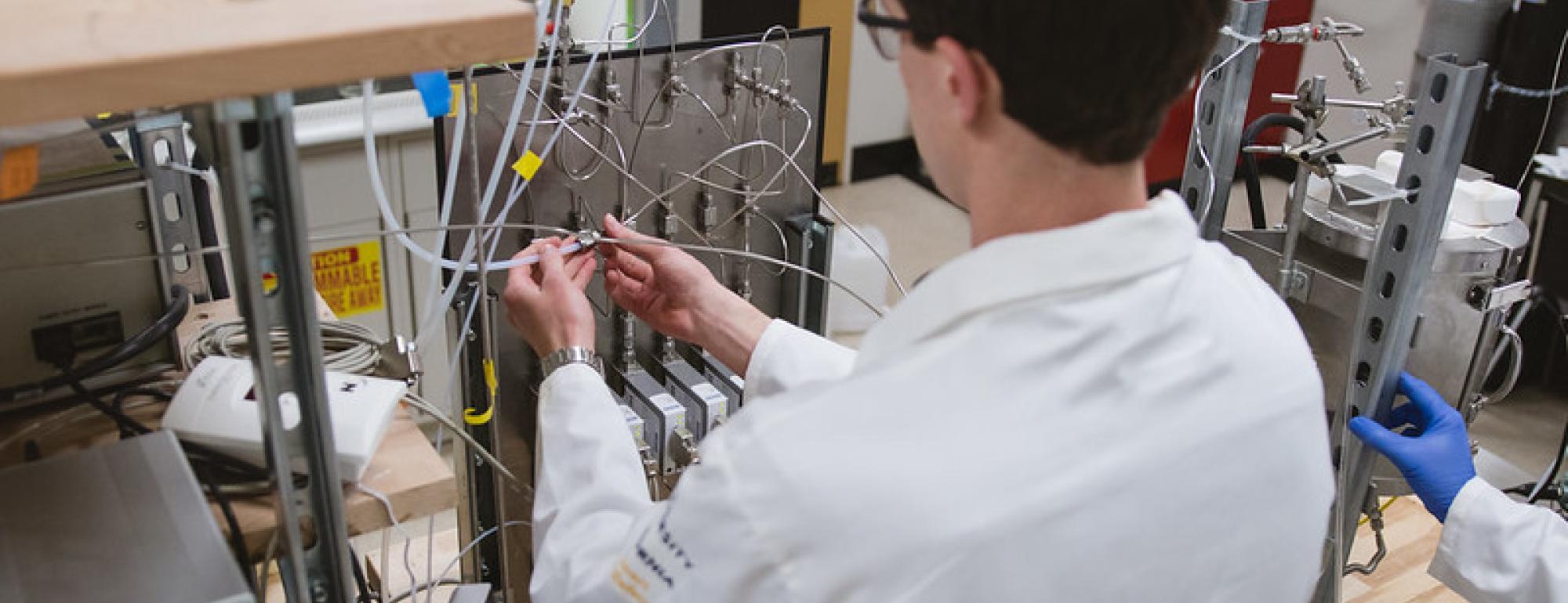 A student in a white lab coat examining equiptment